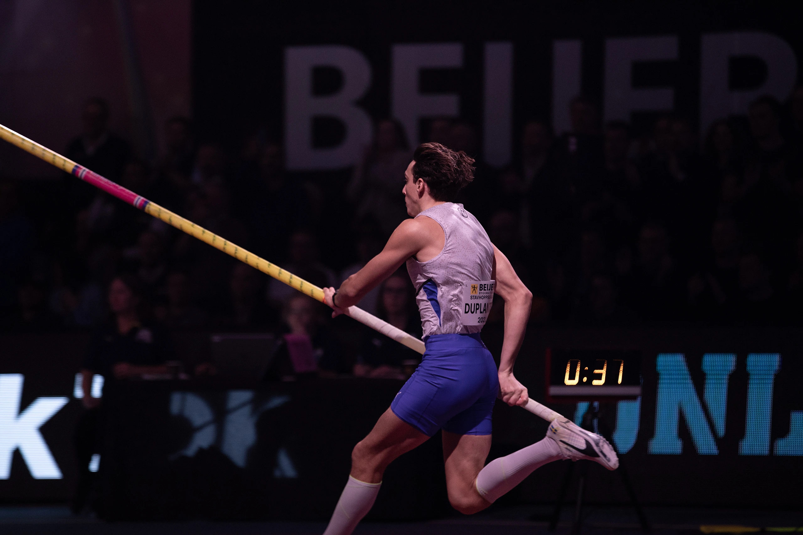 Armand Duplantis i full ansats under Mondo Classic, med stav i hand på väg mot hoppet i en upplyst arena med publik i bakgrunden.