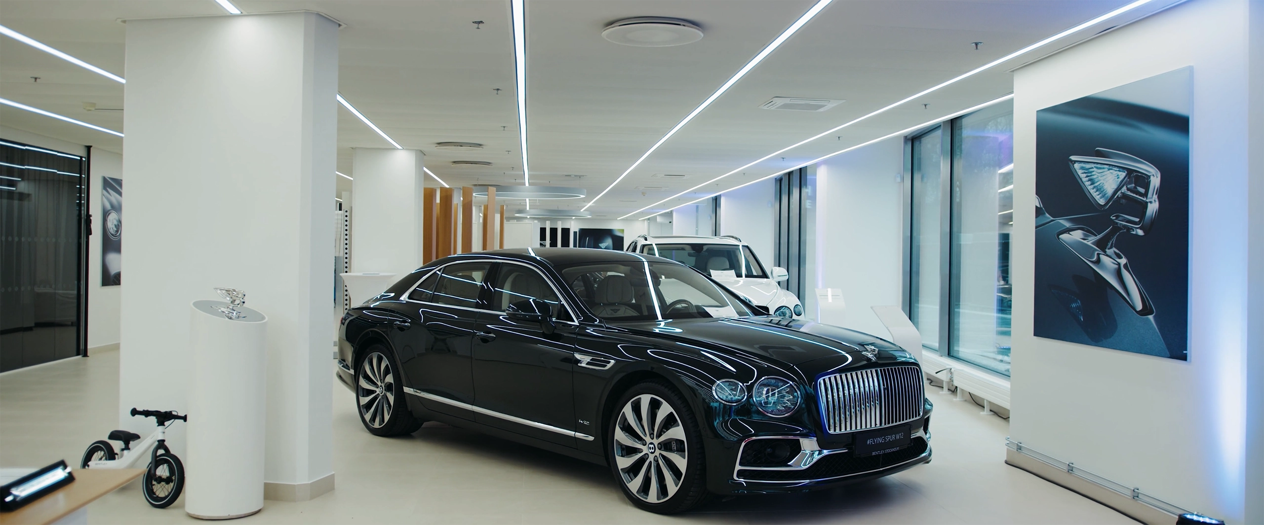 Bentley showroom i Stockholm med svart lyxbil upplyst i en modern, stilren miljö med ljusa ytor, stora fönster och designinslag längs väggarna.