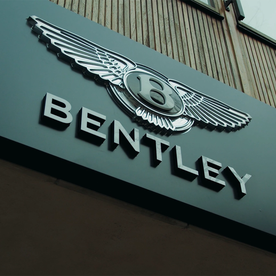 Närbild av Bentleys logotyp och emblem på fasaden utanför showroomet i Stockholm, med den ikoniska vingade symbolen i fokus