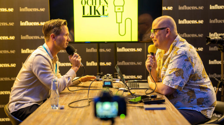 Viktor Frisk spelar in en podcast vid ett bord, med mikrofoner och inspelningsutrustning framför sig, i en studiomiljö med influens.se som bakgrund.