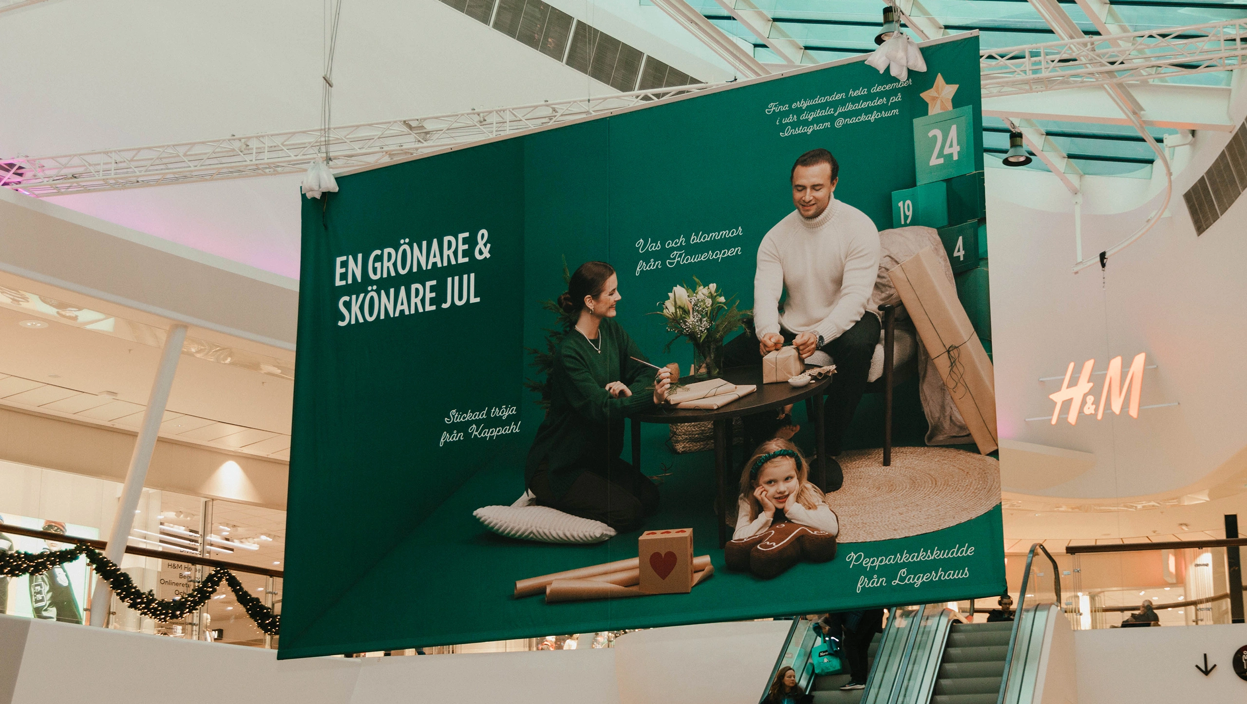 Stor kampanjbanner i Nacka Forum med budskapet “En grönare & skönare jul” – del av julkampanjen med visuell kommunikation och julkalender i centrumet.