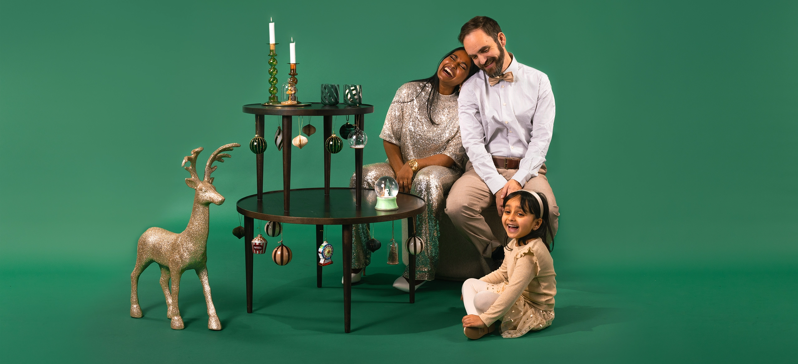 Familj i julig studiofotografering mot grön bakgrund med dekorationer och rekvisita – kampanjbild för Nacka Forums julkampanj.