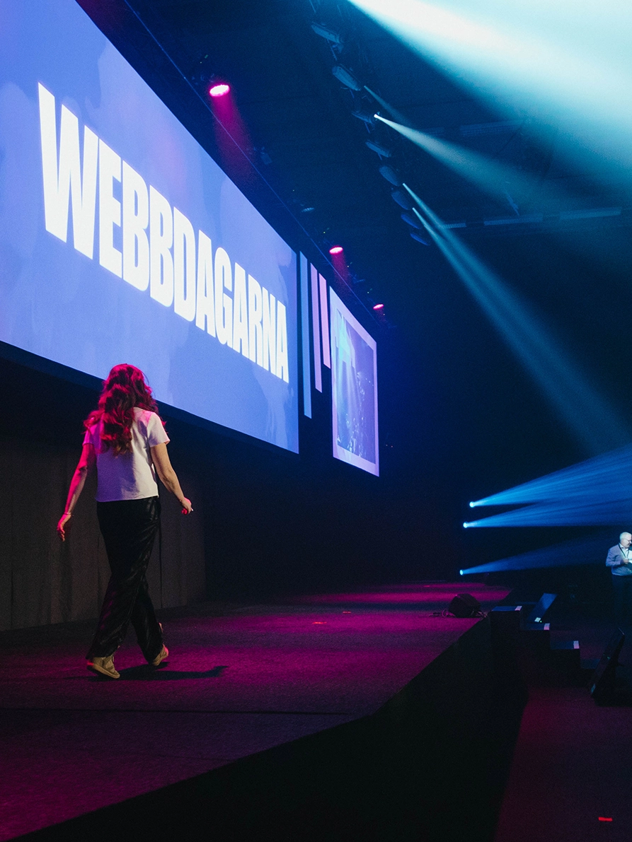 Talare går upp på scen under Webbdagarna med stor LED-skärm i bakgrunden, dramatisk ljussättning och konferensproduktion i Annexet Stockholm