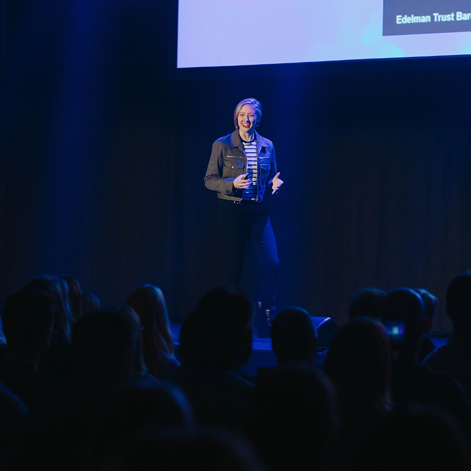 Talare på scen under Webbdagarna med headsetmikrofon, upplyst av scenljus i blå toner under konferens i Annexet Stockholm