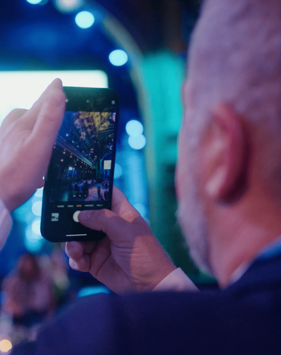 En person fotograferar en scen med mobiltelefon under ett event i blåljusmiljö.