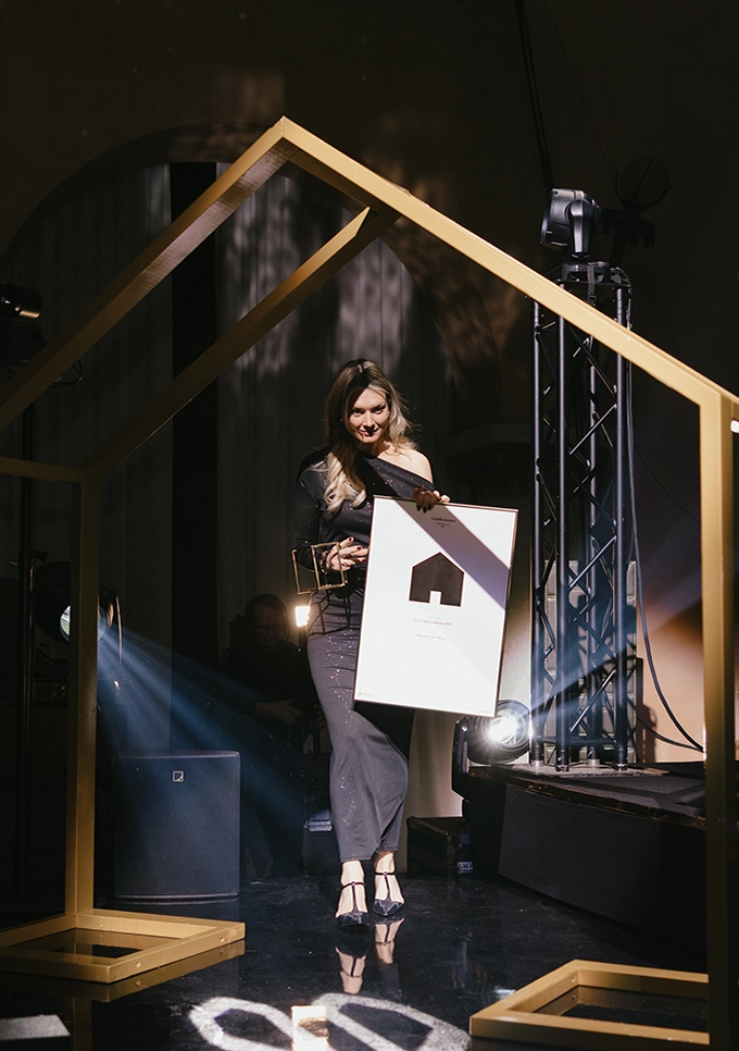 Vinnare på scen under Guldhemmet-galan som tar emot pris, upplyst av scenljus och omgiven av scenografi