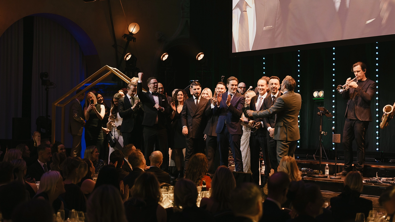 Vinnare och deltagare firar på scen under Guldhemmet-galan med publik, prisutdelning och liveband i bakgrunden