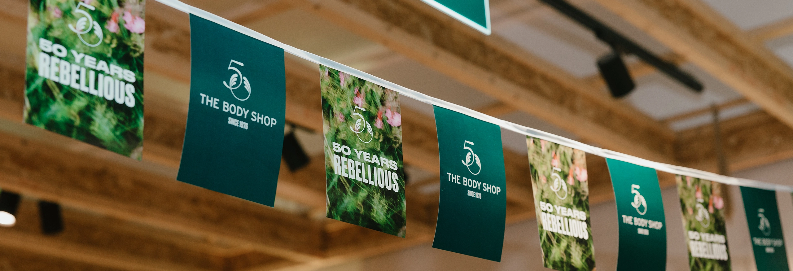 Vimpelgirlang i The Body Shop-butik med budskapet “50 Years Rebellious” och varumärkeslogga som del av jubileumsdekorationen.