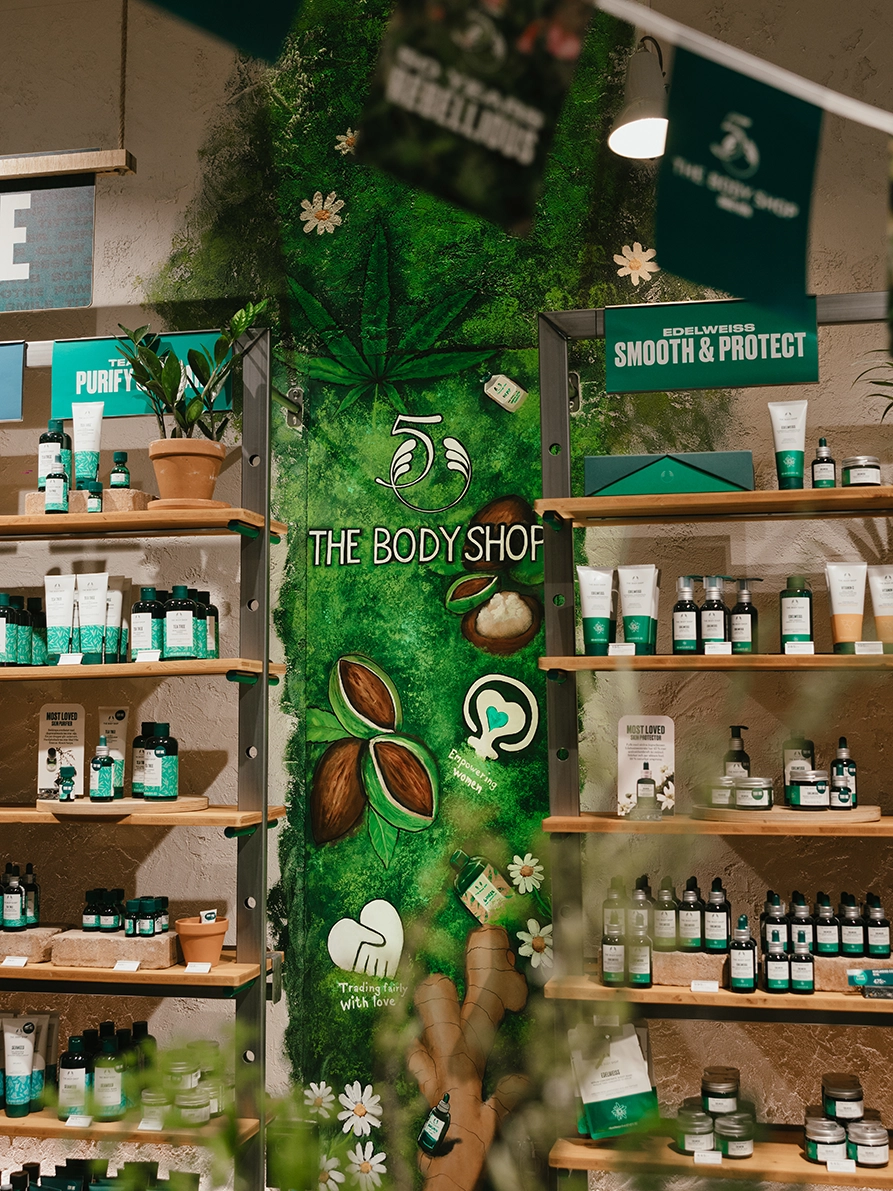 Butiksvägg i The Body Shop med grön muralmålning, varumärkesgrafik och hyllor fyllda med hudvårdsprodukter under 50-årsjubileum.