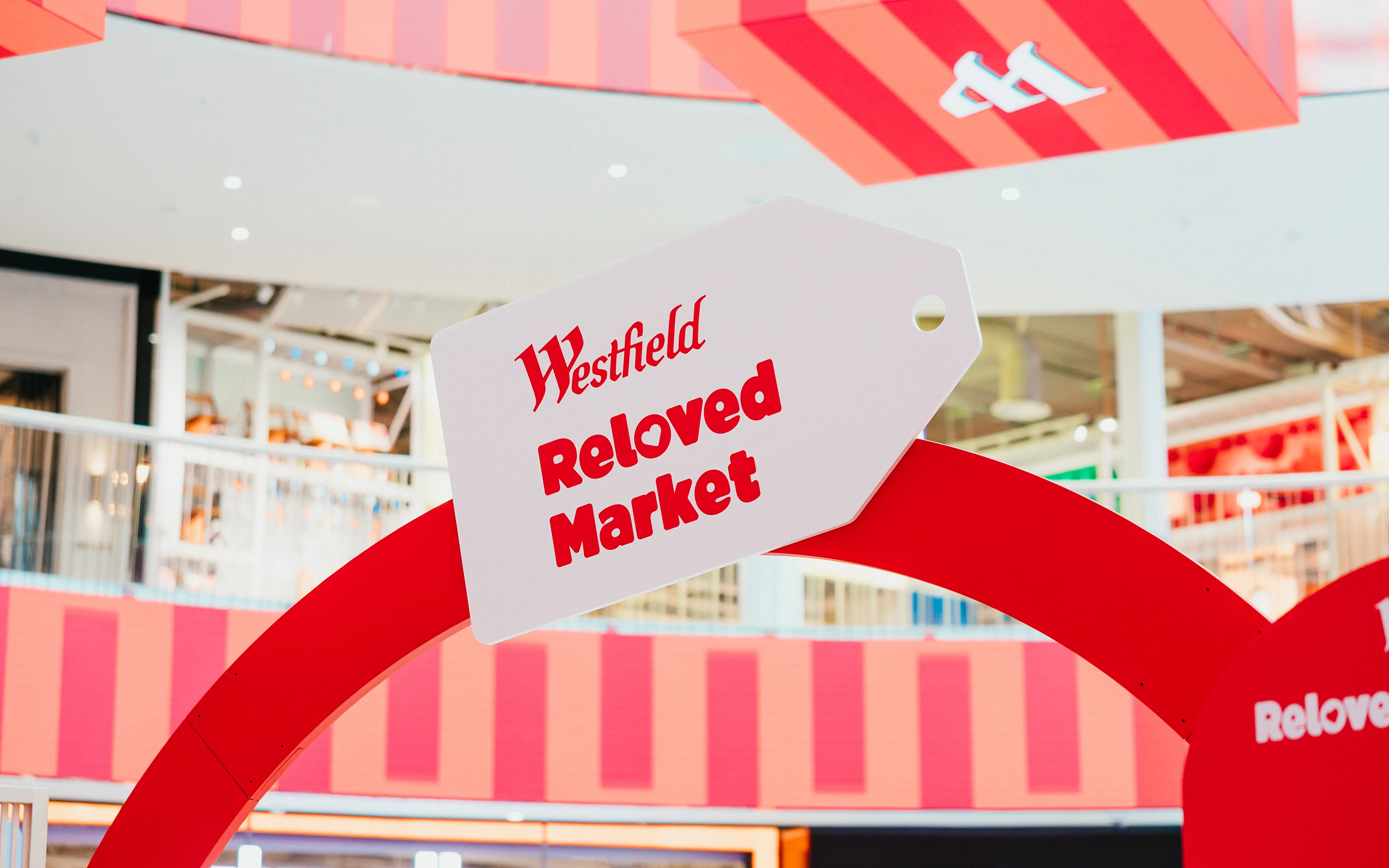 Skylt med texten “Westfield Reloved Market” monterad ovanför eventytan i Mall of Scandinavia, omgiven av grafiska rosa och röda former och retailmiljö i bakgrunden.