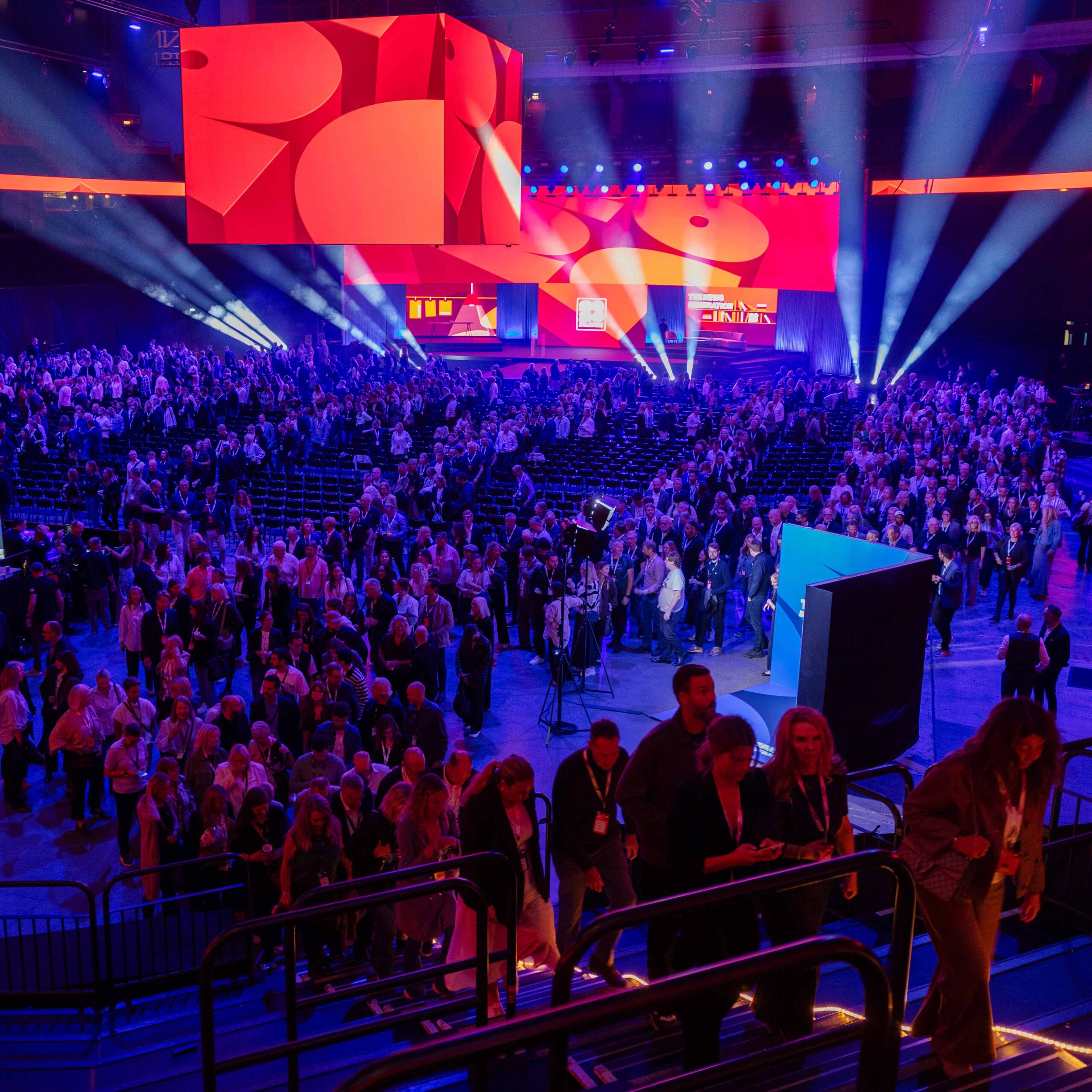 Deltagare i Avicii Arena under The Summit by Bonnier News 2026, med stora skärmar i rött och orange och ljusstrålar över publiken.