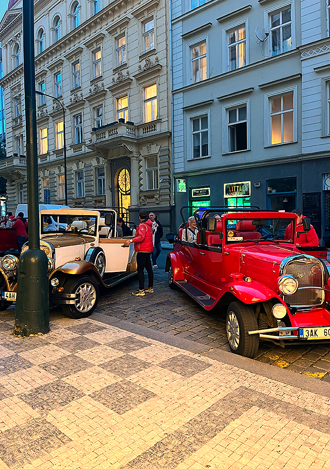 Röda och vita veteranbilar med deltagare på en kullerstensgata under Kvadrats konferensresa i Prag.