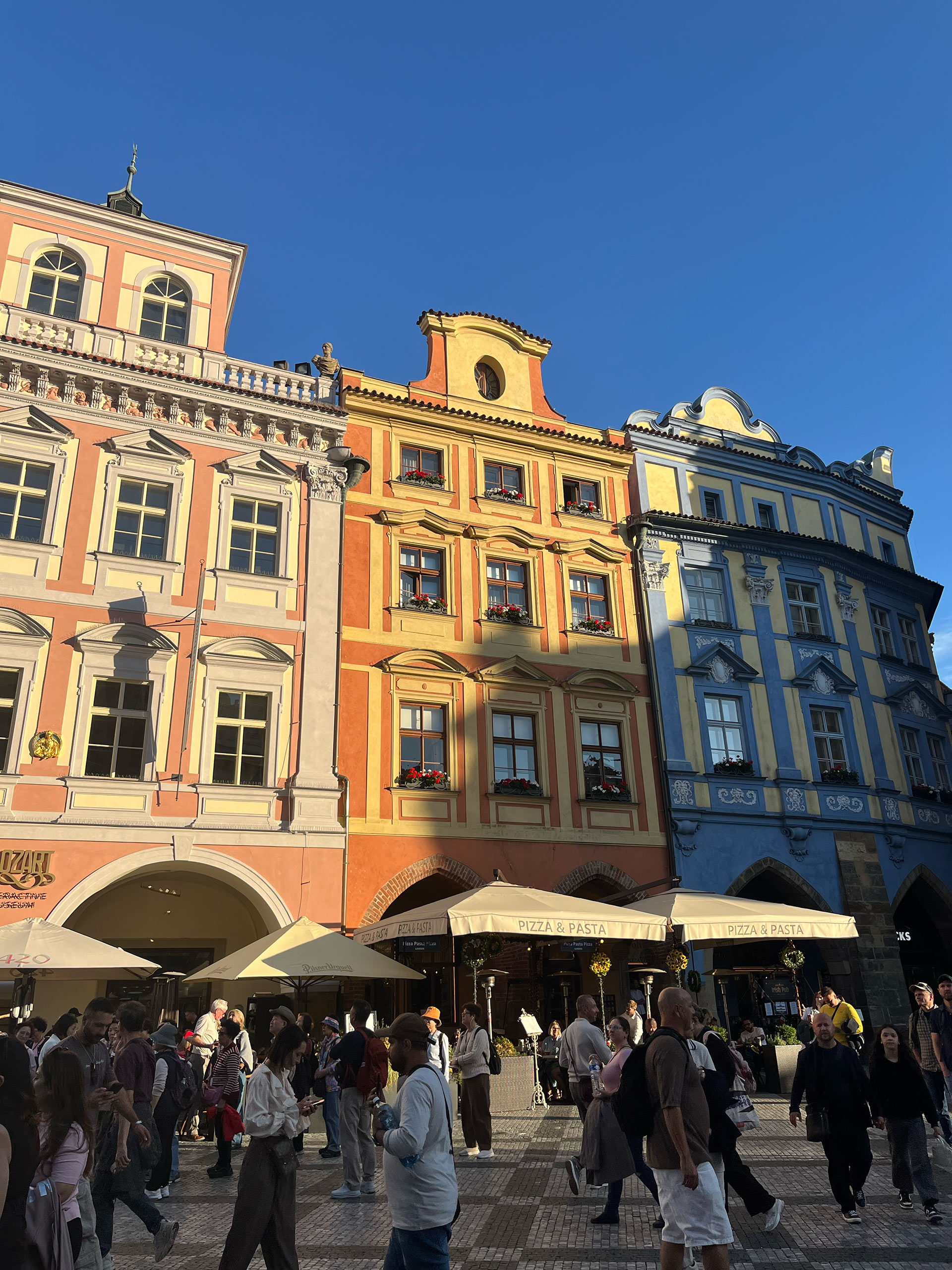 Kvadrat i Prag. Färgglada historiska fasader och uteserveringar med människor på ett soligt torg i Prag.